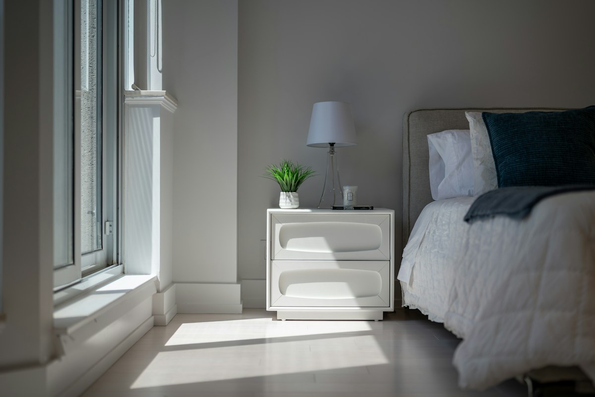 Sunlight entering a furnished bedroom with a bed and nightstand.