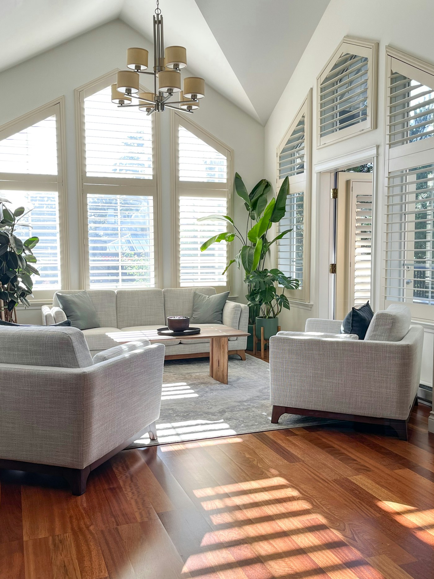 Sunlit living room with seating, plants and several windows